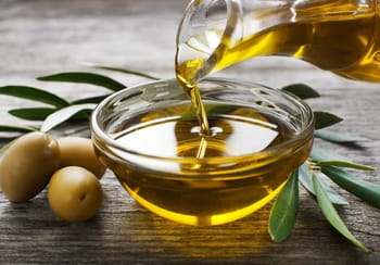 Huile d'olive versée dans un bol en verre avec olives et feuilles d'olivier.