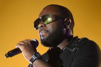 Maître Gims portant des lunettes de soleil noires en performance.