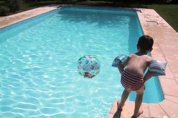 Enfant jouant dans une piscine avec un ballon et un flotteur.