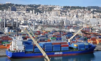 Navire cargo chargé de conteneurs dans un port animé en Algérie.