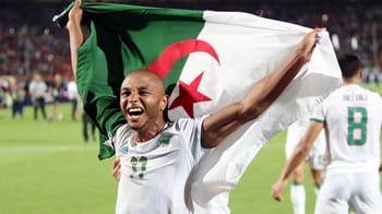 Yacine Brahimi souriant avec le drapeau algérien lors d'un match.