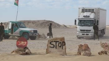 Militaires et véhicules dans un désert avec des panneaux Stop et Stop en arabe.