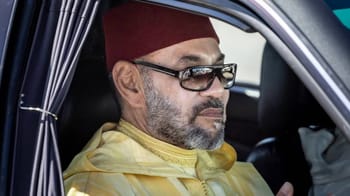 Le Roi Mohammed VI portant un fez et des lunettes dans une voiture officielle.