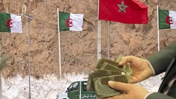 Agent montrant des paquets de drogue avec drapeaux algérien et marocain en arrière-plan.