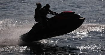 Deux personnes sur un jet-ski en mer, créant des vagues.