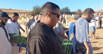 Groupe de personnes en prière lors d'une cérémonie funéraire en plein air.