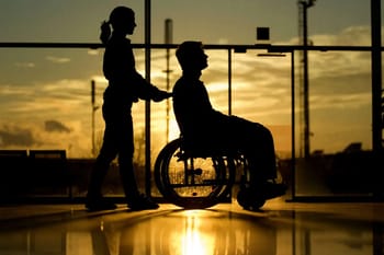 Personne en fauteuil roulant avec aidante dans un aéroport au coucher du soleil.