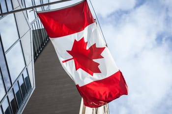 Immigration au Canada : l'arnaque, de plus en plus observée Drapeau du Canada flottant devant un bâtiment moderne.