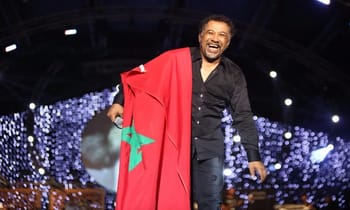 Cheb Khaled avec un drapeau marocain lors d'une performance en scène.