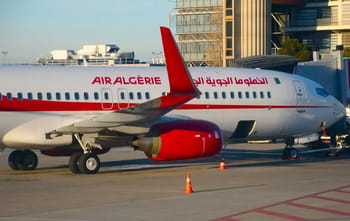 Avion Air Algérie stationné à l'aéroport avec bâtiments modernes en arrière-plan.