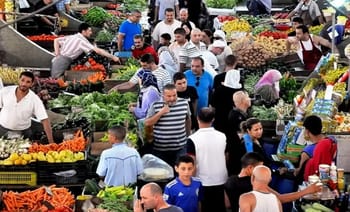 Foule dans un marché algérien avec fruits et légumes colorés.