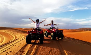 Deux personnes en quad dans le désert avec bras levés.
