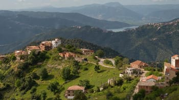 Vue panoramique de villages de Kabylie avec montagnes et lac en arrière-plan.