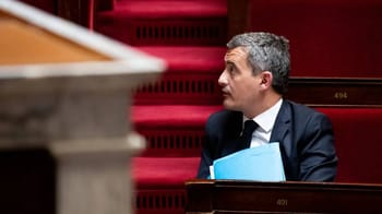 Homme en costume en séance parlementaire avec documents.