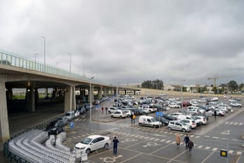 Parking de l'aéroport d'Alger avec voitures et passagers sous un ciel nuageux.