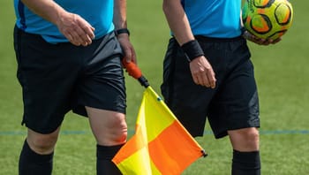 Arbitres de football avec drapeau et ballon sur le terrain.