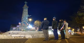 Cérémonie commémorative devant un monument aux morts en soirée.
