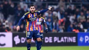 Joueur de football en action sur le terrain avec supporters en arrière-plan.