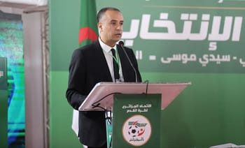 Homme en costume parlant à une conférence de football en Algérie.