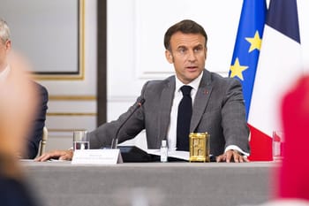 Emmanuel Macron à une réunion officielle avec drapeaux français et européens en arrière-plan.