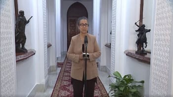 Femme politique parlant devant un micro dans un couloir décoré.