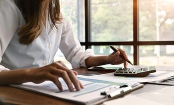 Femme utilisant une calculatrice et un smartphone pour gérer ses finances.