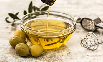Huile d'olive extra vierge dans un bol en verre avec olives vertes.