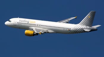 Avion Vueling blanc avec logo jaune en vol dans le ciel bleu.