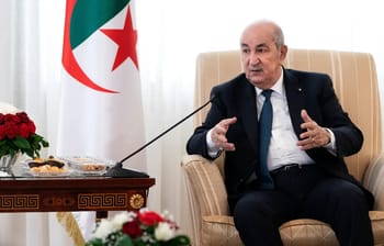 Chef d'État algérien lors d'une réunion diplomatique avec drapeau algérien en arrière-plan.