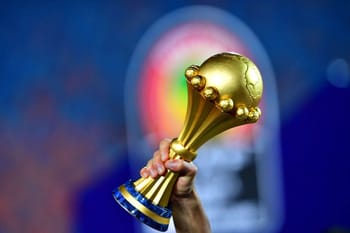 Trophée de la CAN 2025 en or, tenu par une main.
