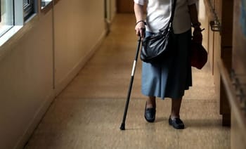Femme âgée avec canne marchant dans un couloir d'hôpital ou de maison de retraite.