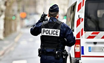 Policier en uniforme avec véhicule de police en arrière-plan.