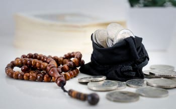 Tasbih, pièces de monnaie et livre religieux sur une table.