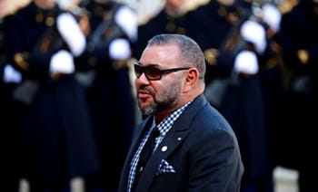 Le Roi Mohammed VI en costume, portant des lunettes de soleil, lors d'une cérémonie officielle.
