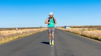 Homme voyageant seul sur une route plate et désertique sous un ciel bleu clair.