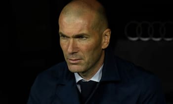 Zinédine Zidane, entraîneur de football, en pleine réflexion lors d'un match.