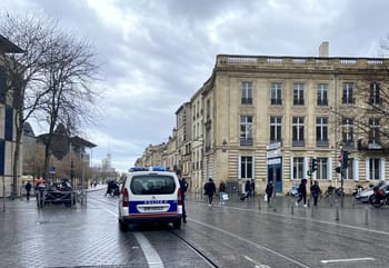 Vue de la rue à Bordeaux avec un véhicule de police et des passants.