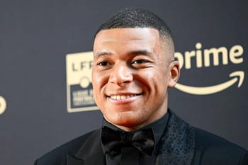Kylian Mbappe souriant en costume noir et nœud papillon.