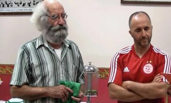 Deux hommes lors d'une réunion, l'un avec une barbe blanche et l'autre en maillot de football.