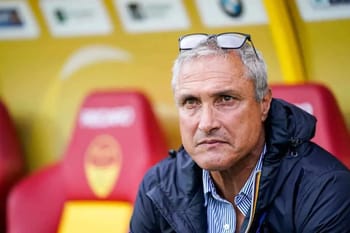 Homme d'âge moyen, regard sérieux, lunettes sur la tête, assis dans un stade de football.