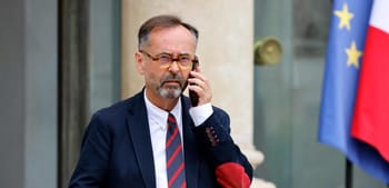 Homme en costume parlant au téléphone devant drapeaux français et européen.