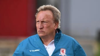Entraîneur de football âgé portant un blouson bleu avec logo.