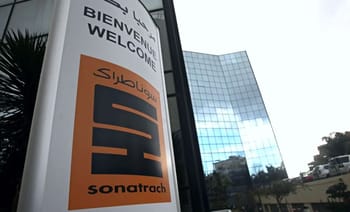 Entrée de Sonatrach avec panneau multilingue et bâtiment moderne en arrière-plan.