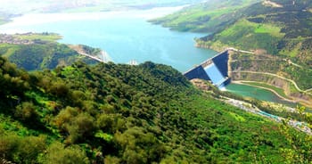 Le barrage de Béni Haroun, rempli après de fortes pluies, entouré de verdure et de montagnes.