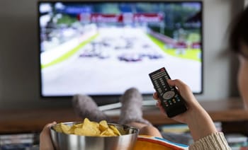 Personne regardant la télévision avec une télécommande et un bol de chips.