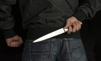 Personne tenant un couteau derrière un pantalon.
