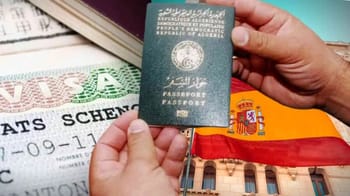 Main tenant un passeport algérien avec drapeau espagnol en arrière-plan.
