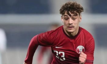 Jeune joueur de football algérien portant maillot rouge en pleine course.