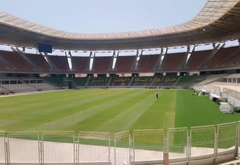 Stade de Douera vide avec pelouse bien entretenue et tribunes modernes.