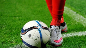 Joueur de football avec ballon sur le terrain vert.